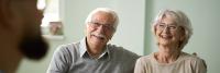 Elderly couple smlies while listening to surgeon speak during office visit.